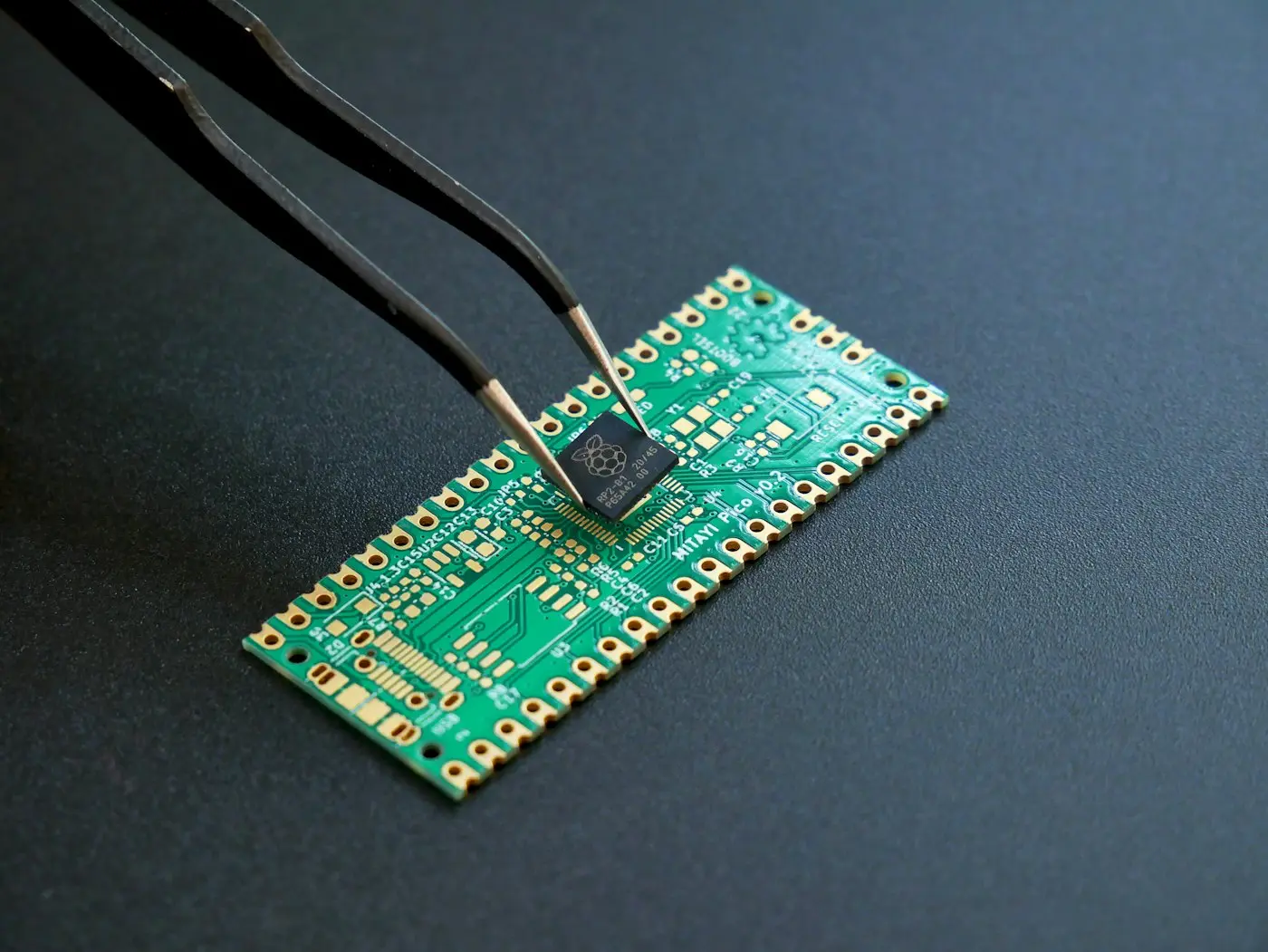 Tweezers placing a microchip on a green circuit board