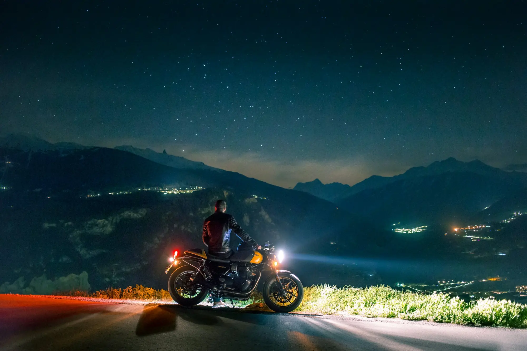 Motorcyclist stopped on a mountain road at night, headlight on